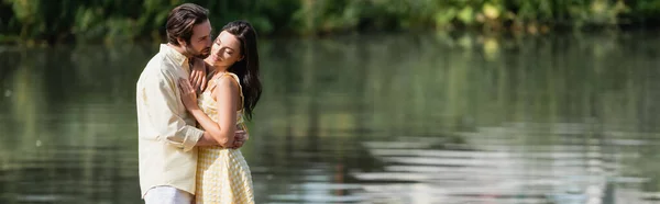 Jeune couple en vêtements d'été étreignant près de la rivière, bannière — Photo de stock