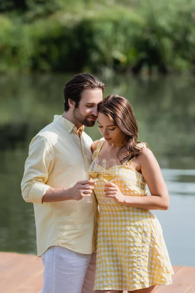 Young couple in summer clothes holding glasses with wine near river — Stock Photo