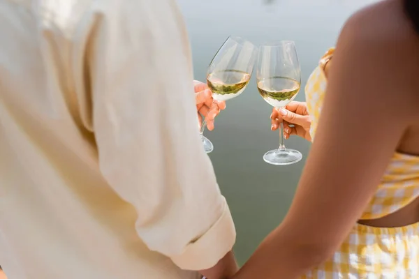 Cropped view of romantic couple clinking glasses with wine near lake — Stock Photo