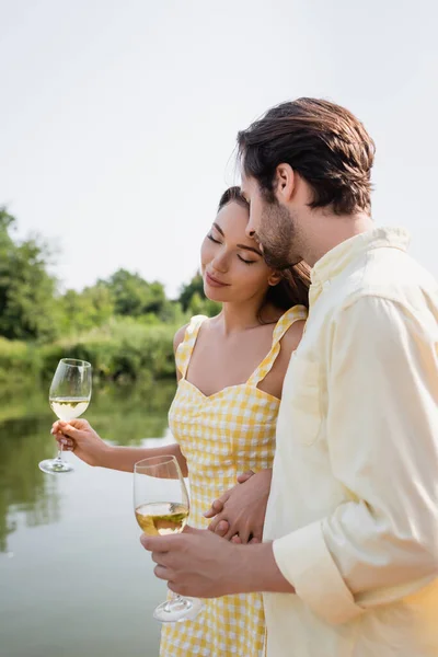 Romantic couple holding glasses with wine near river — Stock Photo
