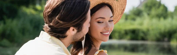 Verschwommener Mann flüstert lächelnde Frau mit Strohhut ins Ohr, Banner — Stockfoto