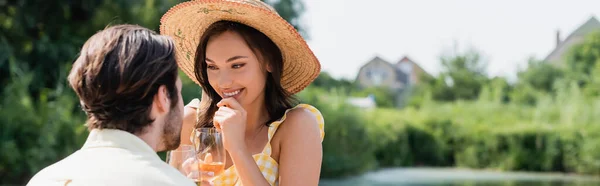 Femme excitée dans un chapeau de paille tenant un verre de vin et regardant petit ami, bannière — Photo de stock