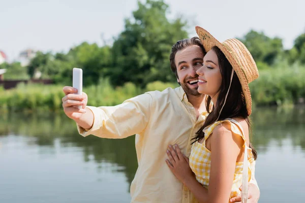 Happy young couple taking selfie near lake — Stock Photo