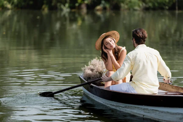 Femme rêveuse en chapeau de paille regardant petit ami romantique pendant la promenade en bateau — Photo de stock