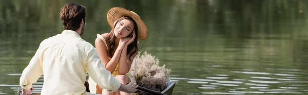 Mujer de ensueño en sombrero de paja mirando novio romántico durante el paseo en barco, bandera - foto de stock