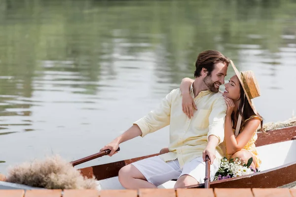 Joyeuse jeune femme en chapeau de paille étreignant l'homme heureux lors d'un voyage romantique en bateau — Photo de stock