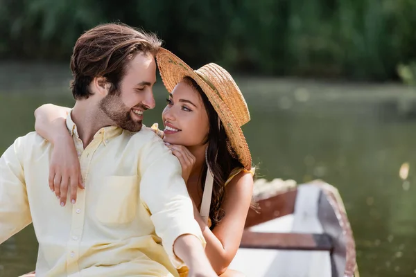 Усміхнена молода жінка в солом'яному капелюсі обіймає щасливого чоловіка під час романтичної подорожі на човні — стокове фото