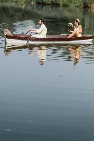 Side view of happy woman holding flowers and having romantic boat ride with man — Stock Photo