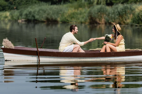 Vue latérale de la femme heureuse tenant la main avec l'homme pendant la promenade en bateau — Photo de stock