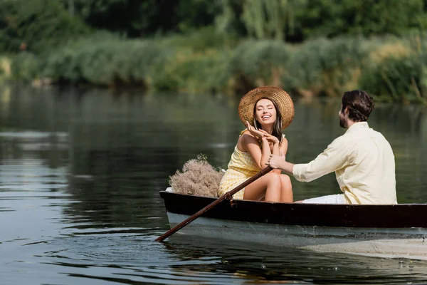 Smiling woman in straw hat having romantic boat ride with man — Stock Photo