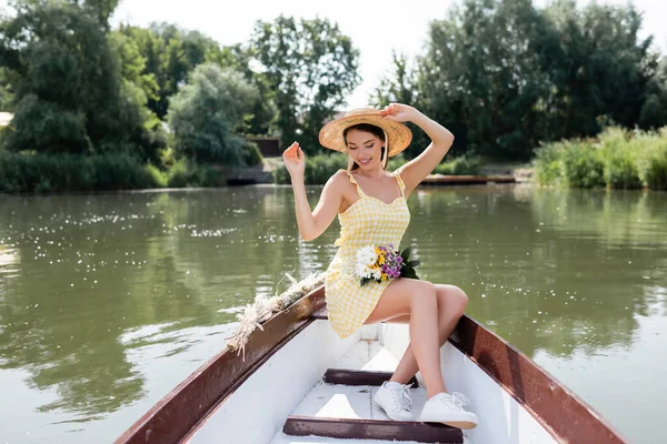 Feliz jovem mulher ajustando chapéu de palha e ter passeio de barco no lago — Fotografia de Stock