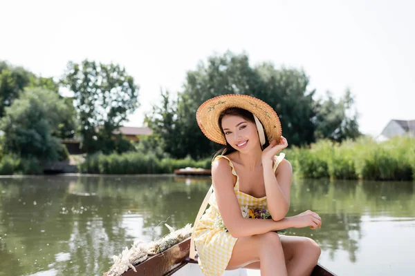 Sorrindo jovem mulher em chapéu de palha e vestido ter passeio de barco no lago — Fotografia de Stock