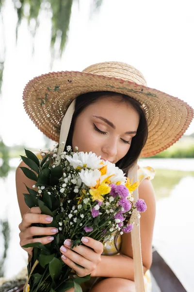 Junge Frau mit Strohhut, die nach Blumen riecht — Stockfoto