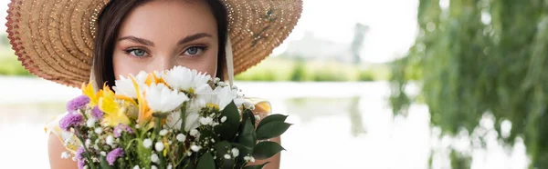 Young woman in straw hat covering face while smelling flowers, banner — Stock Photo