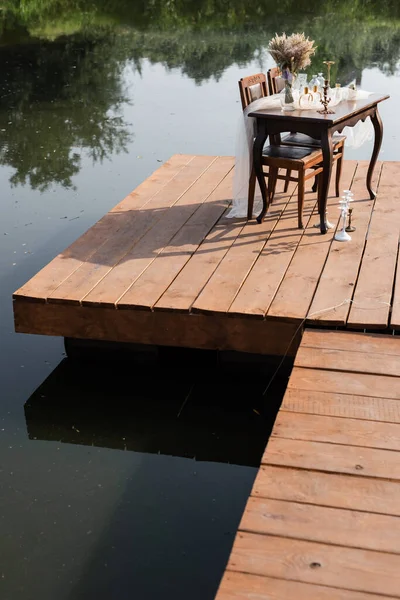 Romantico tavolo apparecchiato per la cena sul molo di legno vicino al lago — Foto stock