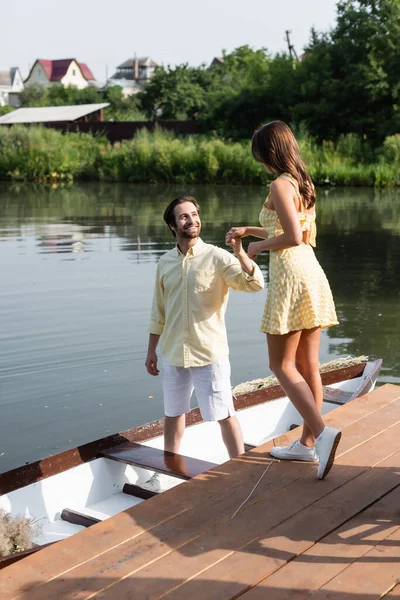 Happy bearded man in summer clothes holding hands with girlfriend near boat — Stock Photo