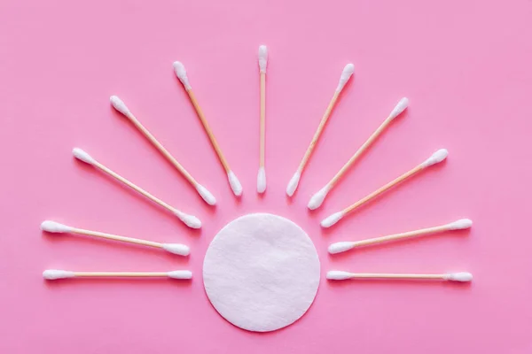 Flat lay of ear sticks around white cotton pad on pink background, top view — Stock Photo
