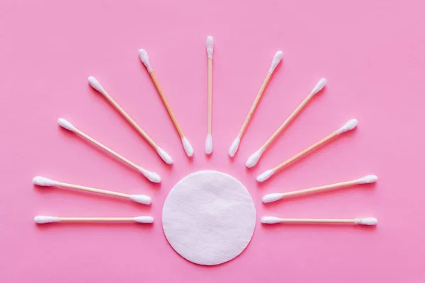 Posa piatta di bastoncini per le orecchie intorno al cuscinetto di cotone bianco su sfondo rosa, vista dall'alto — Foto stock