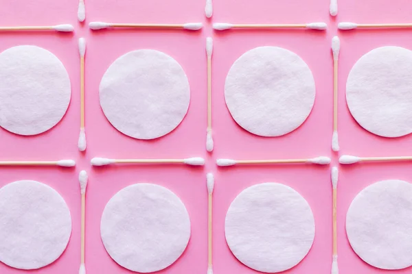 Flat lay of white cotton pads and ear sticks on pink background, top view — Photo de stock