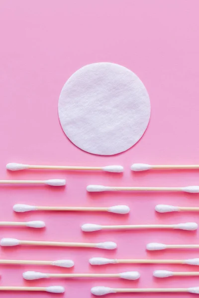 Almohadilla de algodón blanco por encima de las filas de palos de la oreja sobre fondo rosa, vista superior - foto de stock