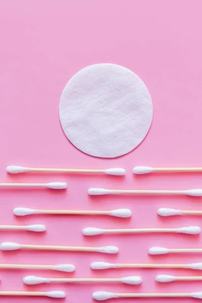 White cotton pad above rows of ear sticks on pink background, top view — Fotografia de Stock