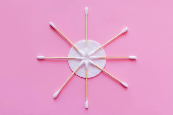 Leigos planos de paus de ouvido cosméticos perto de algodão branco almofada no fundo rosa, vista superior — Fotografia de Stock