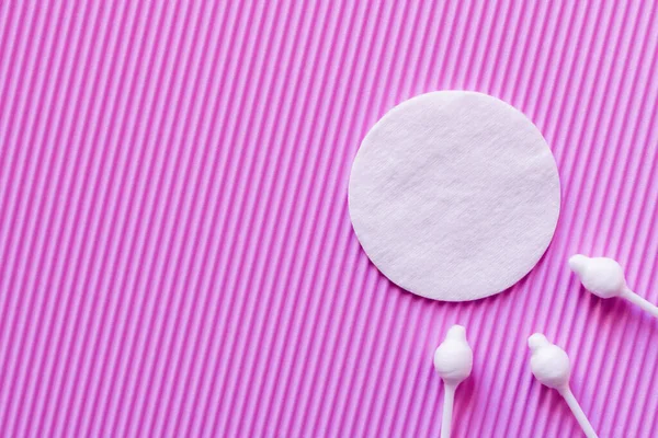 Top view of cotton pad and ear sticks on purple textured background - foto de stock