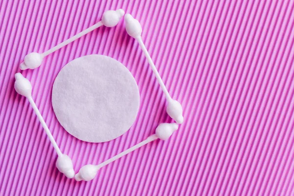 Top view of white cotton pad in frame of ear sticks on purple textured background - foto de stock