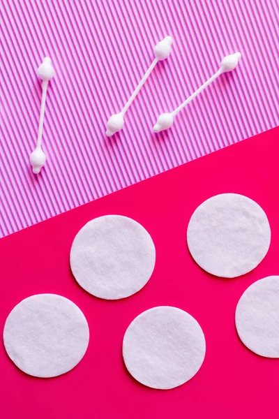 Vista dall'alto dei cuscinetti in cotone bianco e dei bastoncini per le orecchie su sfondo bicolore rosa e viola — Foto stock