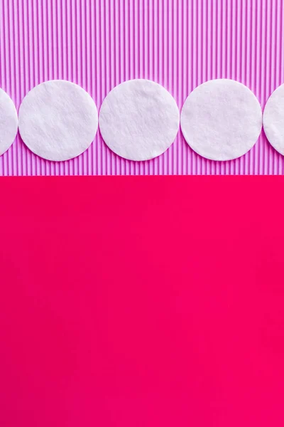 Horizontal row of cotton pads on bicolor violet and pink background, top view — Foto stock