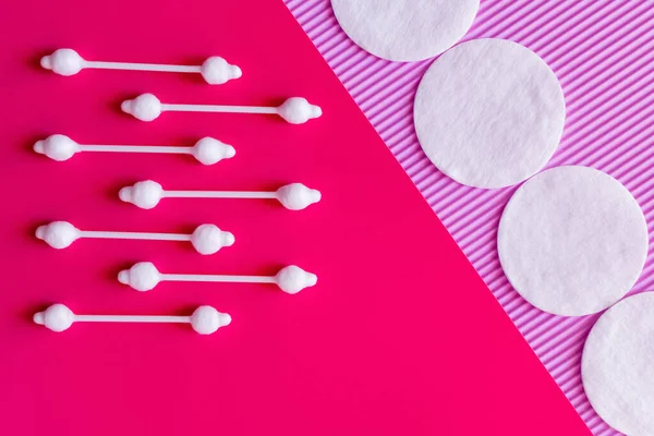 Flat lay of ear sticks and cotton pads on pink and violet textured background, top view - foto de stock