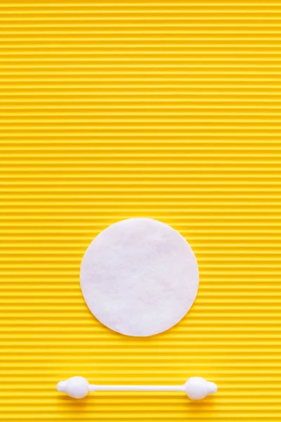 Top view of white cotton pad and ear stick on yellow textured background - foto de stock