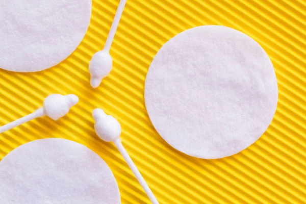 Close up of white cotton pads and ear sticks on yellow textured background, top view — Fotografia de Stock
