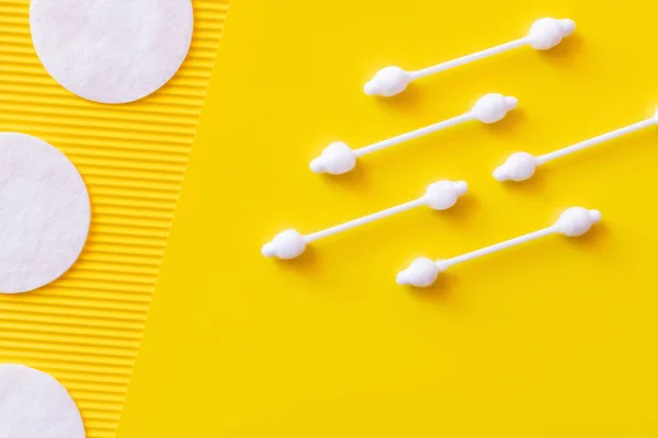 Vista superior de orejeras higiénicas y almohadillas de algodón cosmético sobre fondo texturizado amarillo - foto de stock