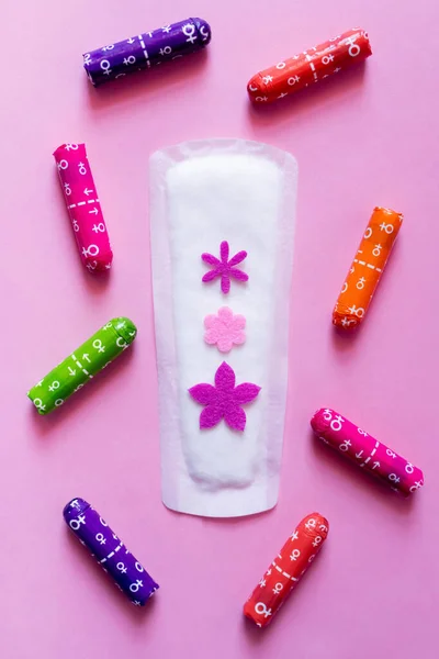 Top view of panty liner with decorative flowers near packed tampons on violet background — Stockfoto