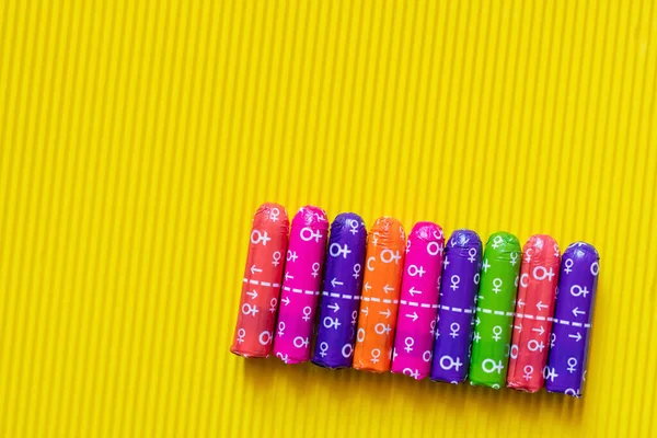 Vista superior de tampones en embalaje multicolor con signos femeninos sobre fondo texturizado amarillo - foto de stock