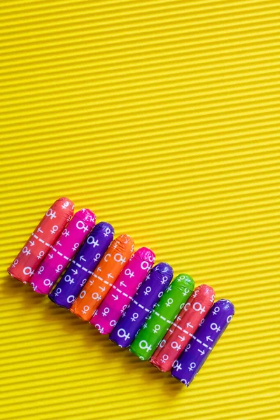 Top view of packed multicolored tampons with female signs on yellow textured background — Stock Photo