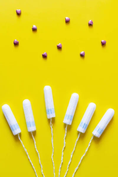 Top view of tampons near decorative hearts on yellow background — стоковое фото