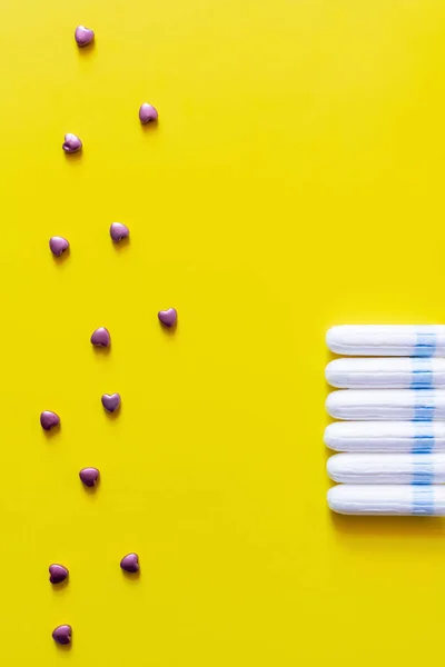 Top view of decorative hearts near row of tampons on yellow background — Stockfoto