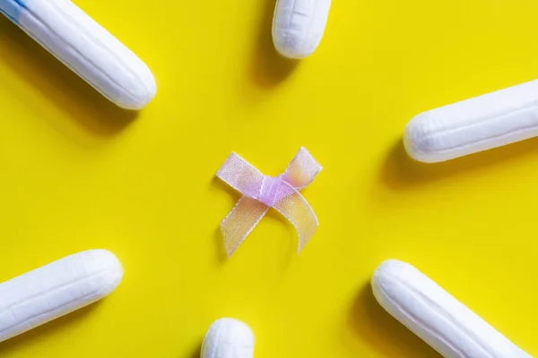 Top view of white tampons around bow on yellow background — стоковое фото