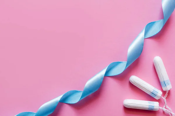 Vue du dessus du ruban de satin bleu près des tampons sur fond rose — Photo de stock