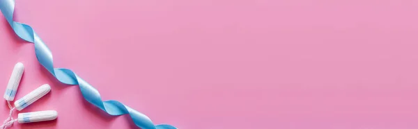 Вид зверху бавовняних тампонів біля синьої атласної стрічки на рожевому фоні, банер — стокове фото