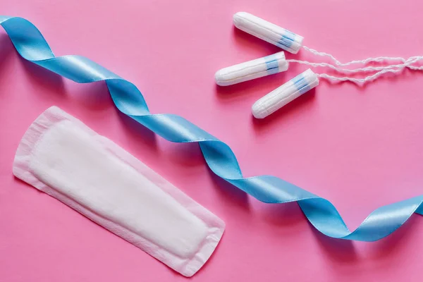Top view of tampons and soft panty liner near blue satin ribbon on pink background — Foto stock