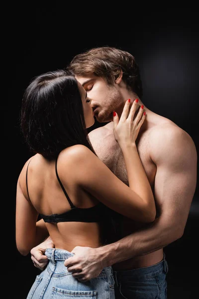 Чуттєва жінка в бюстгальтері цілує хлопця на чорному тлі — стокове фото