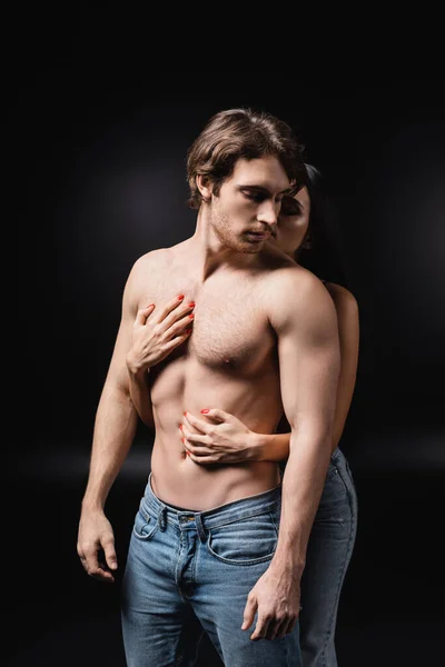 Young woman touching torso of sensual boyfriend on black background — Stock Photo