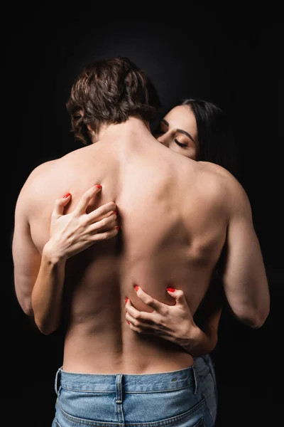 Brünette Frau kratzt Rücken von Mann ohne Hemd isoliert auf schwarz — Stockfoto