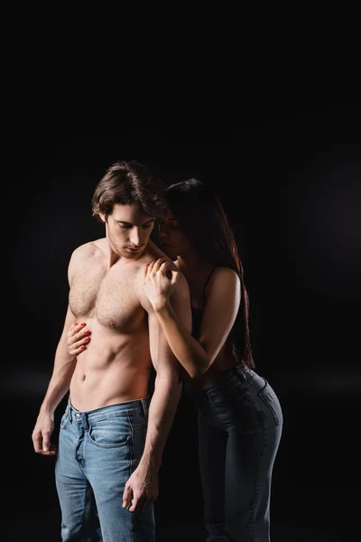 Young woman in jeans touching sexy boyfriend isolated on black — Fotografia de Stock