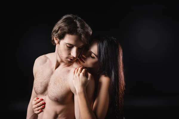 Femme séduisante embrassant l'homme musculaire isolé sur noir — Photo de stock