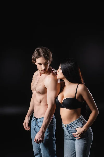 Sensual woman in jeans and bra looking at boyfriend on black background — Stock Photo