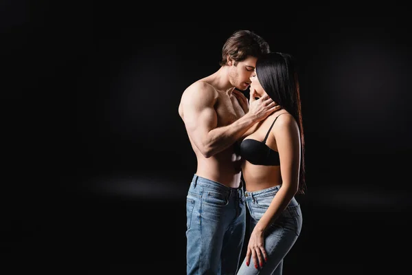 Sexy man in jeans touching girlfriend in bra on black background — Stock Photo